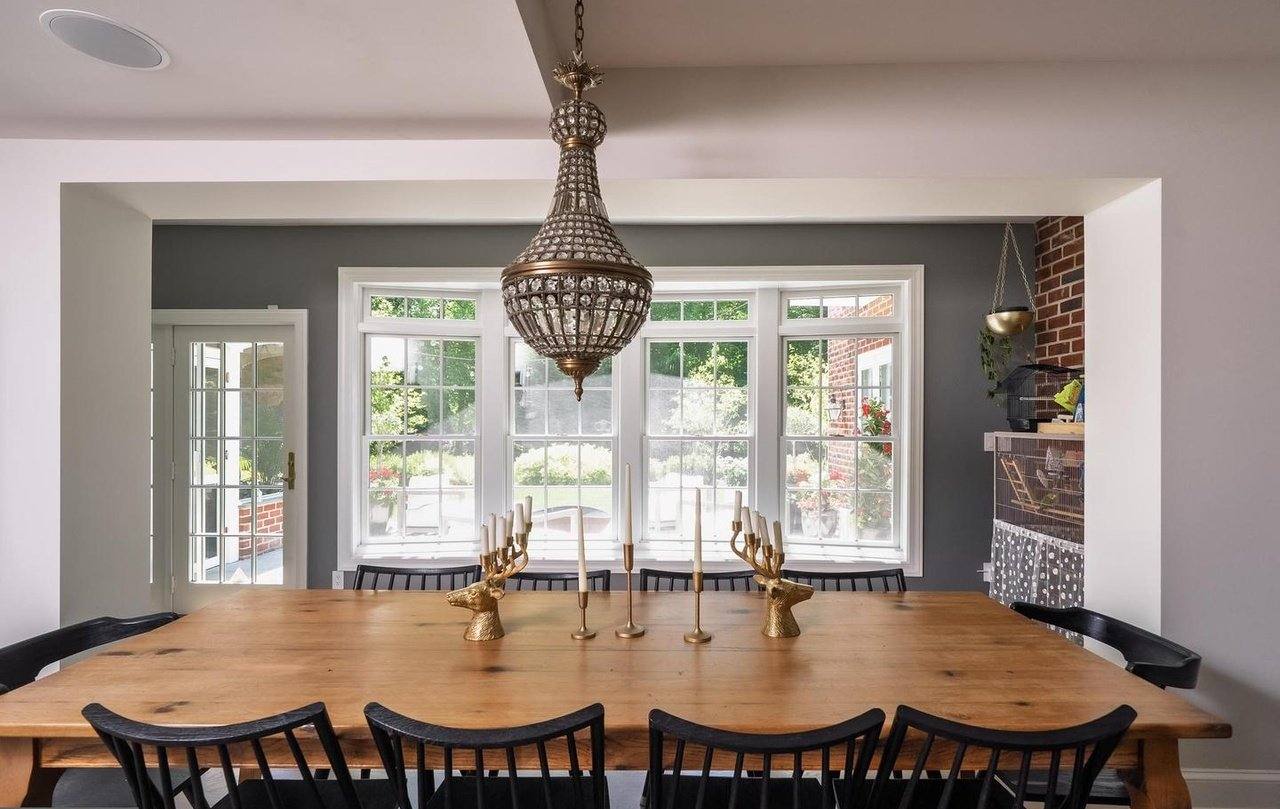 Dining room with a long wood table, chandelier and a wide bay window