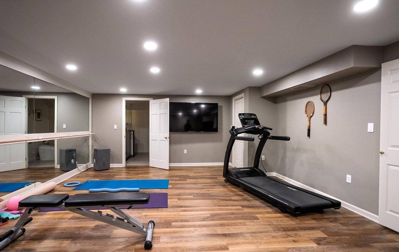 Finished home gym with a treadmill, bench, mirrored wall and wood-look flooring